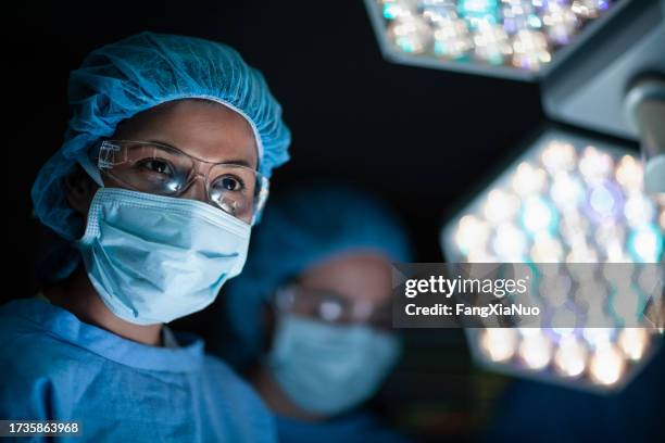 un médecin hispanique souriant à une infirmière dans une salle d’opération chirurgicale avec des collègues et des lumières à l’hôpital - chirurgien photos et images de collection