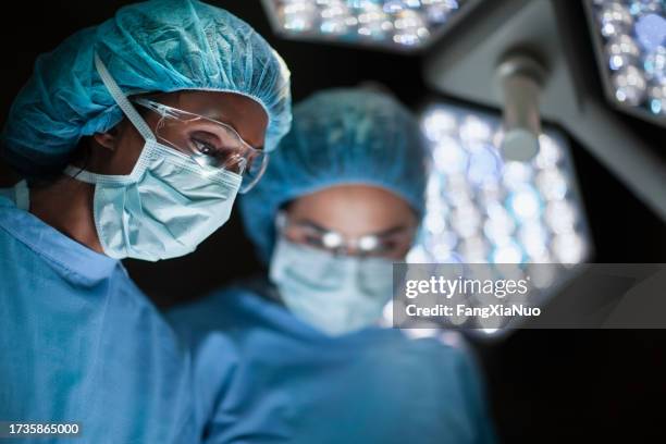 medico e infermiera di etnia indiana asiatica che guardano in basso al paziente nella sala operatoria di chirurgia in ospedale con le luci - chirurgo foto e immagini stock