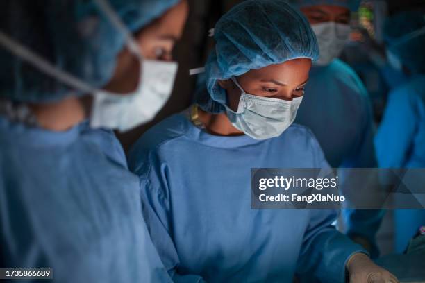 infermiera ispanica del medico professionista medico che guarda in basso seria nella concentrazione verso il paziente nella sala operatoria di chirurgia in ospedale con i colleghi - sala operatoria foto e immagini stock