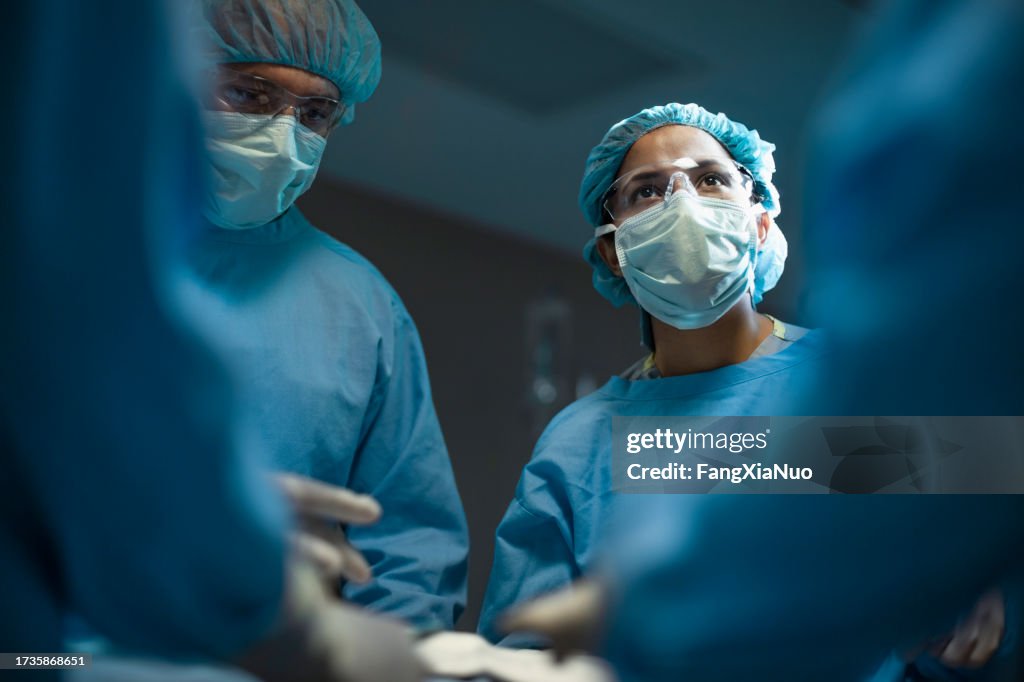 Hispanic medical professional doctor nurse looking upward during surgery operation procedure in hospital with colleagues