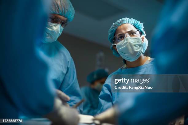 hispanic medical professional doctor nurse looking serious towards colleagues during surgery operation procedure in hospital - cirurgião imagens e fotografias de stock