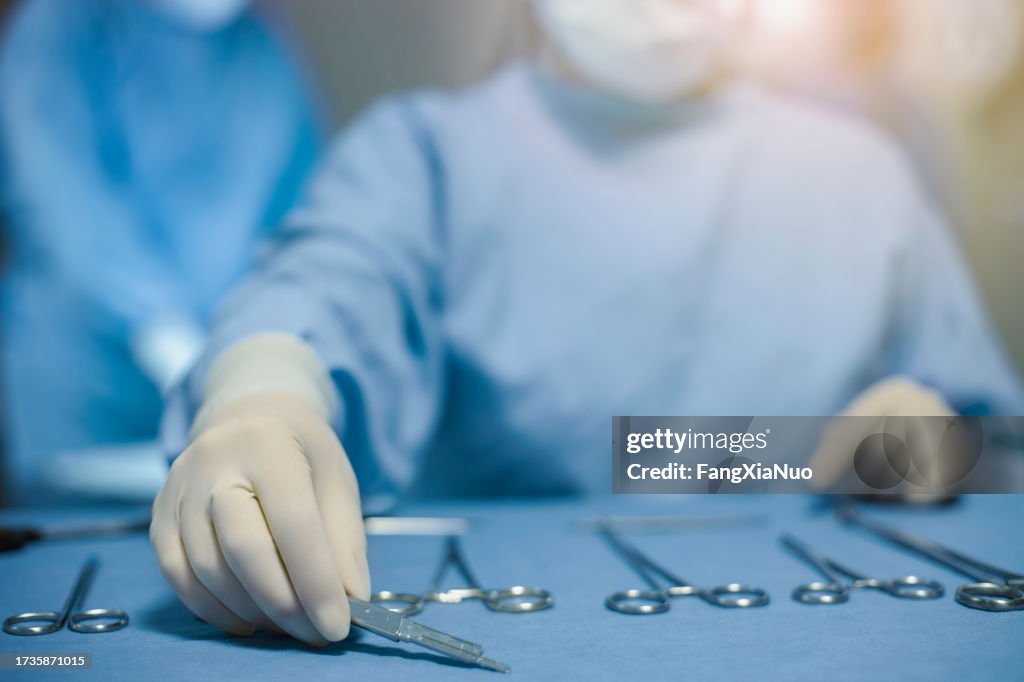 Mano dell'infermiera che prepara la disposizione degli strumenti medici chirurgici sul vassoio che indossa guanti in lattice indumenti da lavoro protettivi per la sicurezza in sala operatoria chirurgica in ospedale con medico medico infermiere
