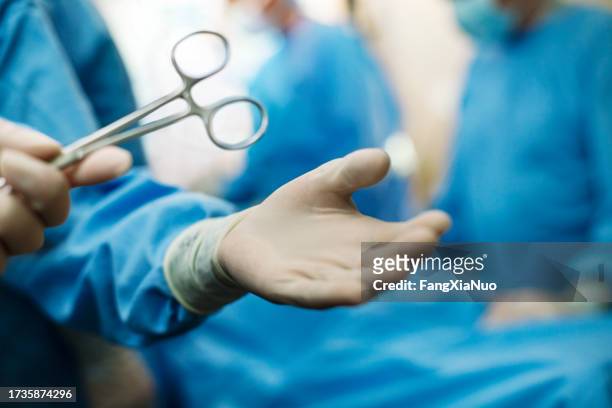 hand of nurse passing medical tool to doctor palm of hand wearing protective workwear in medical surgery operation room in hospital with patient incidental people background - surgery tools stock pictures, royalty-free photos & images