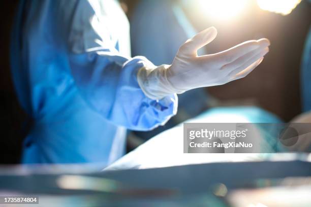 hand of medical professional doctor surgeon wearing protective workwear latex glove reaching to colleague nurse in support care and teamwork in surgery operation room in hospital with colleagues and light - wonder stockfoto's en -beelden