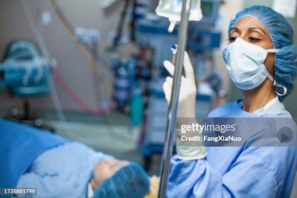 multiracial hispanic black ethnicity woman nurse doctor checking iv drip medication for patient in surgery operating room in hospital wearing protective workwear anesthesiologist - anaesthetic stock pictures, royalty-free photos & images