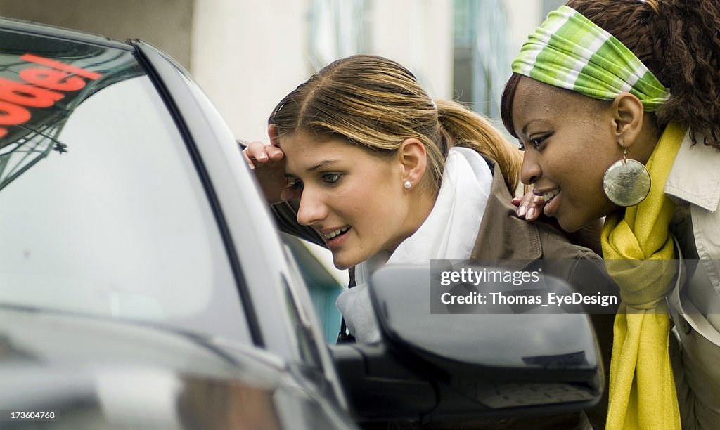 Two young women shopping for a new car, looking in window