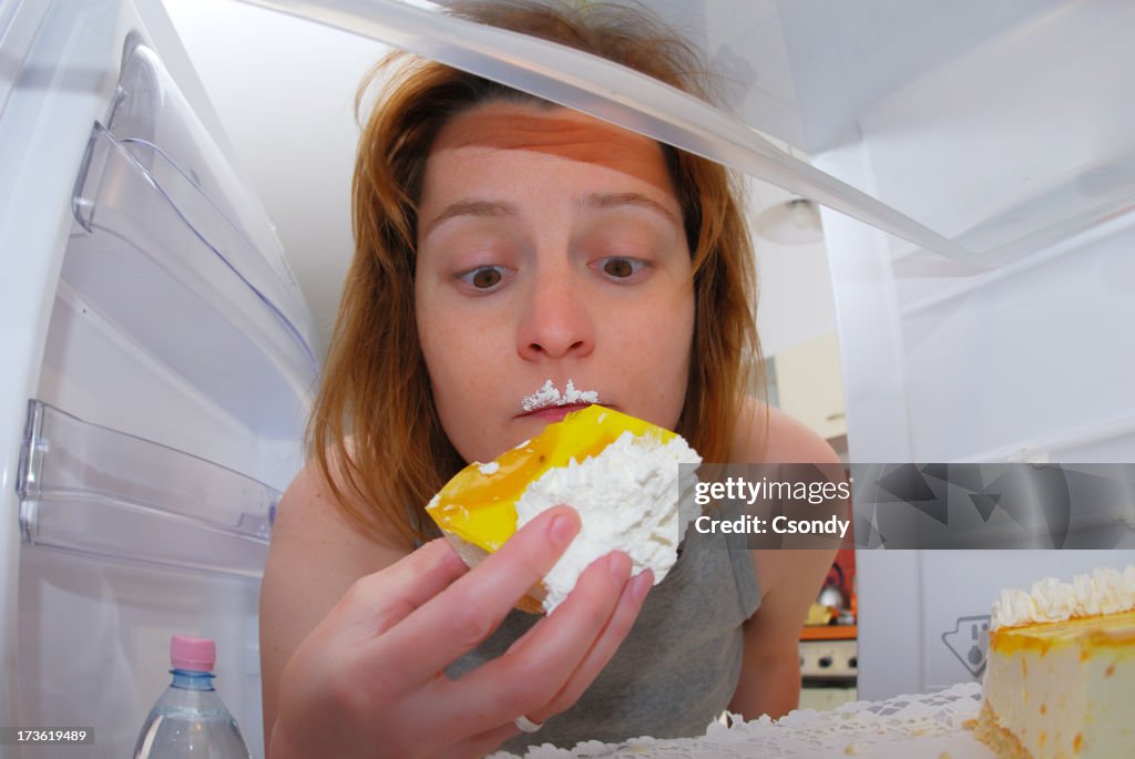 Junge Frau isst Kuchen aus dem Kühlschrank.