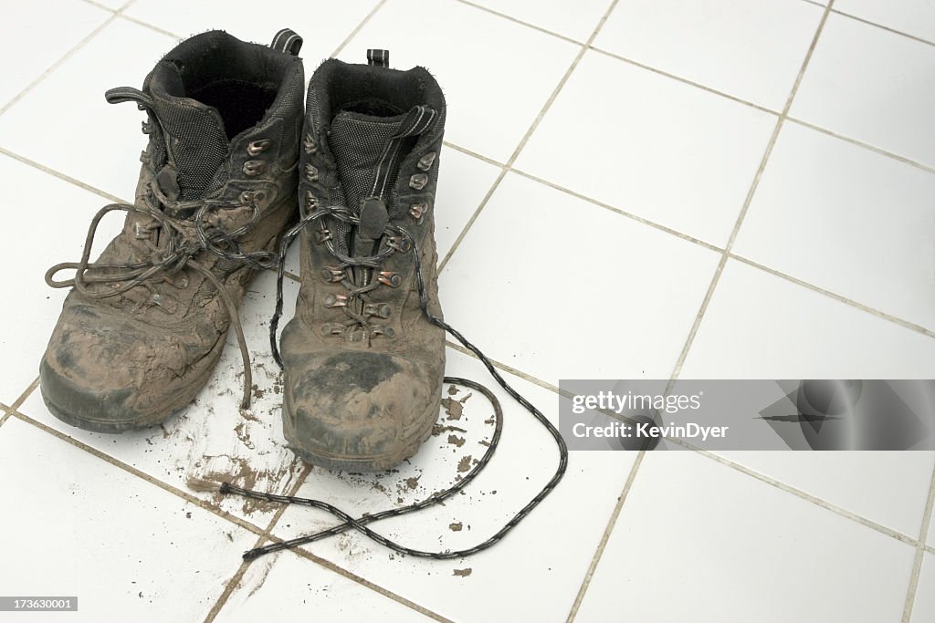 Muddy hiking boots leaving dirt on clean white tiles