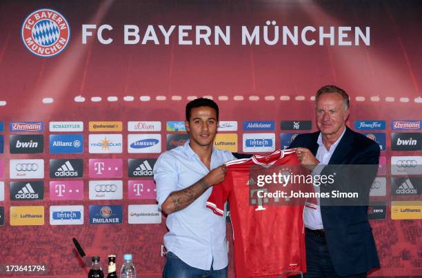 Thiago Alcantara of FC Bayern Muenchen presents his new match jersey with FCB managing director Karl-Heinz Rummenigge after a press conference at...