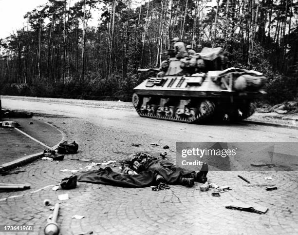 Tank of the Sixth Armored Division, Third US Army, speeds past two dead Nazi bazooka gunners lying surrounded by scattered equipment as it heads...