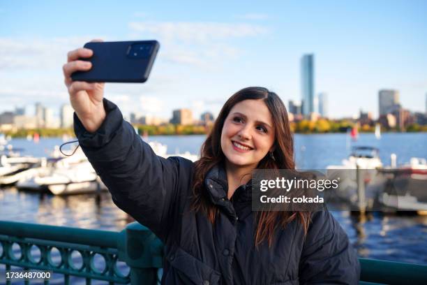 mulher usando celular para tirar uma selfie em boston - rio charles - fotografias e filmes do acervo