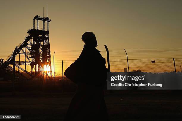 Woman walks past a derelict gold mine shaft's winding gear in front of the setting sun on July 15, 2013 in Johannesburg, South Africa. Johannesburg...