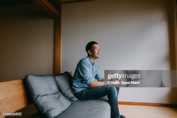 man sitting on sofa and looking outside from home - asian man sitting at desk stock pictures, royalty-free photos & images