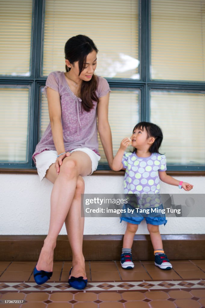 Young mom talking to toddler girl on window sill