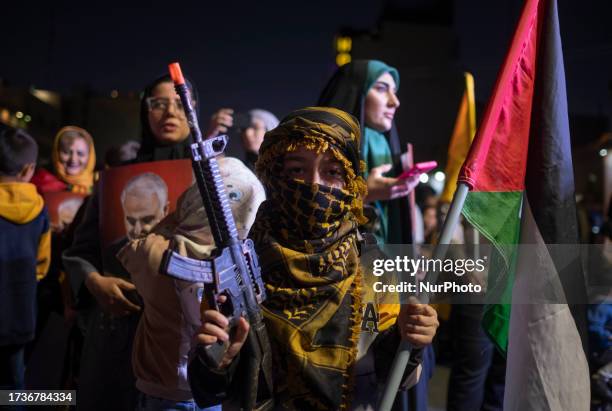 Young Iranian boy wearing a Palestinian scarf carrying a rifle and a Palestinian flag while taking part in a rally protesting the Israeli attacks on...