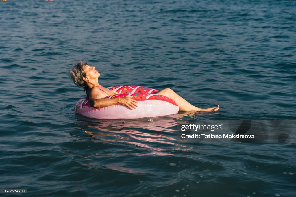 A pension-aged woman has fun riding the waves in an inflatable pink circle donut.