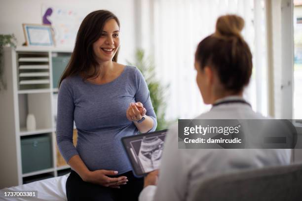 lächelnde schwangere frau bei einer konsultation mit einem arzt in der klinik - obgyn stock-fotos und bilder