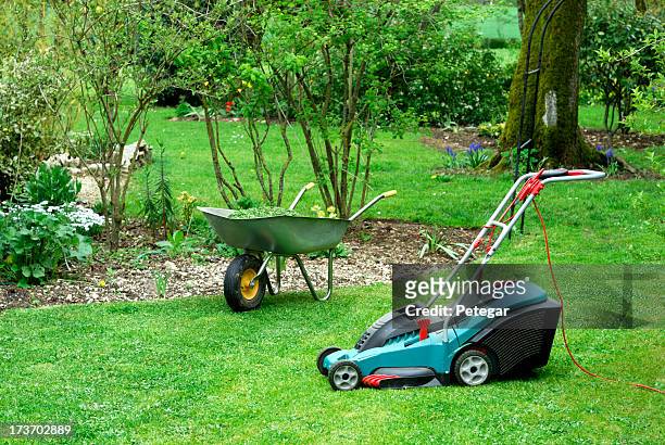 electric rasenmäher und schubkarre in einem garten - lawnmower stock-fotos und bilder
