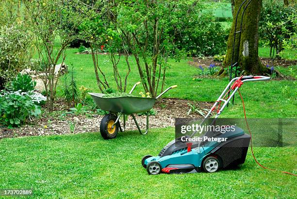 electric lawn mower and wheelbarrow in a garden - gräsklippning bildbanksfoton och bilder