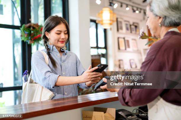 digital payments can increase transaction speeds in your business. a female customer using a smartphone pays a bill by tapping to pay through the card-swiping machine at a cashier counter in a retail store. digital payment and digital banking technology. - personalised communication stock-fotos und bilder