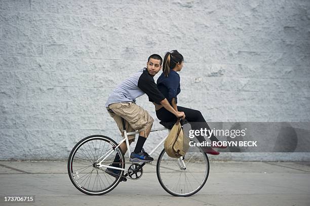 Young man looks back at protestors as he rides down the street with a girl on the handlebars, in downtown Los Angeles, July 16, 2013. Protestors...