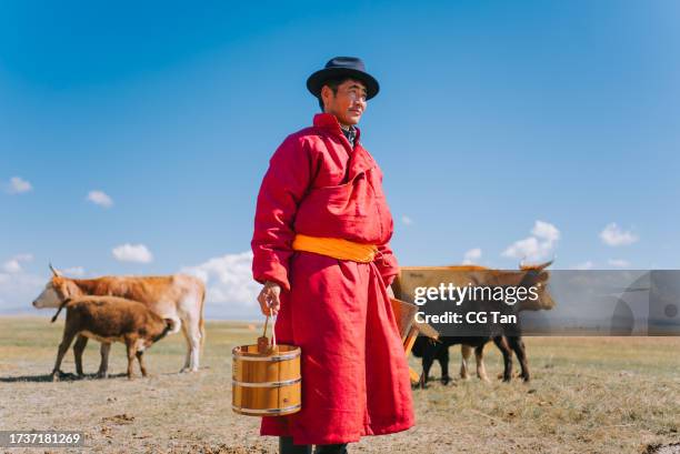 mongolian man carrying milk bucket looking away standing on pasture - mongoolse etniciteit stockfoto's en -beelden