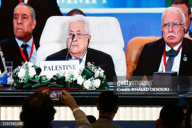Journalists watch a large screen showing Palestinian President Mahmud Abbas attending the International Peace Summit hosted by the Egyptian president...