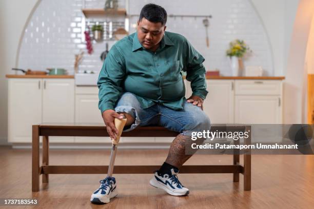 moment of unwavering determination and resilience as a man adjusts his prosthetic leg in the kitchen. a car accident took his leg, but it couldn't break his spirit. adjusting his prosthetic, showcasing his confidence and self-sufficiency. - amputee stock pictures, royalty-free photos & images