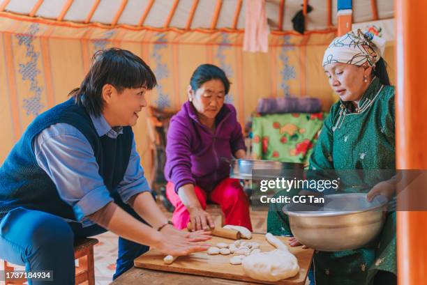 asian chinese female tourist learning preparing mongolian traditional dumpling buuz with local mongolian women in yurt kneading - independent mongolia stock pictures, royalty-free photos & images