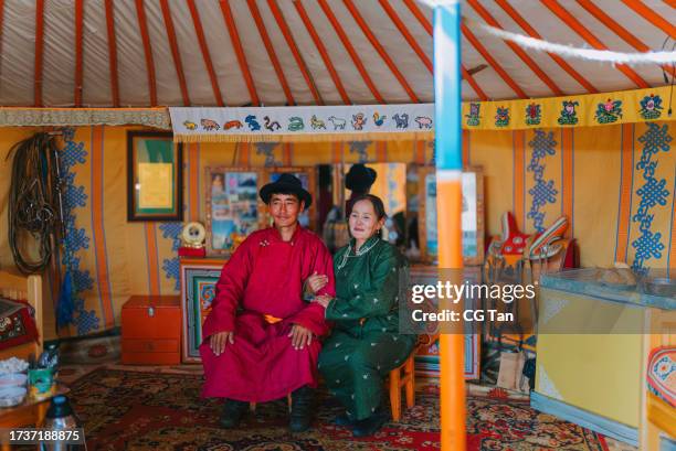 portrait of mongolian nomad couple with traditional clothing sitting inside ger, yurt - mongoolse etniciteit stockfoto's en -beelden