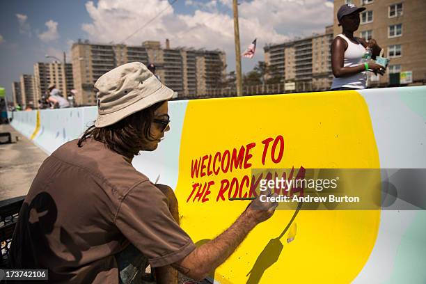 Artist John Garcia paints a mural along a roadway barrier on July 17, 2013 in the Rockaway neighborhood of the Queens borough of New York City. The...