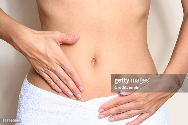 a woman touching her stomach wearing a white towel - waist stockfoto's en -beelden