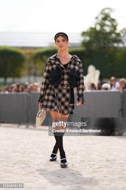 Negin Mirsalehi wears a headband, a beige and black checked jacket with black large pockets, a pleated mini skirt, a white Lady Dior bag, knee high...