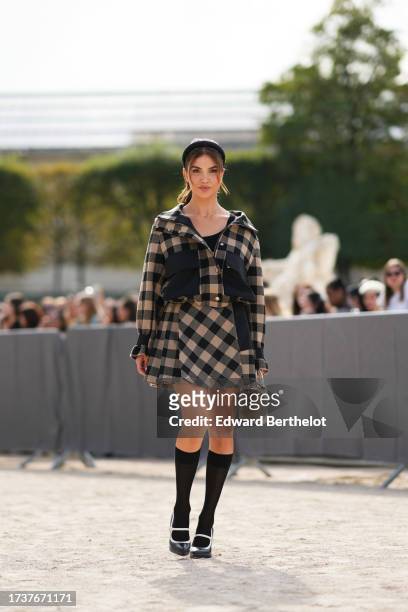 Negin Mirsalehi wears a headband, a beige and black checked jacket with black large pockets, a pleated mini skirt, a white Lady Dior bag, knee high...