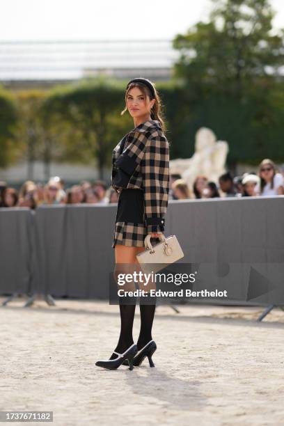 Negin Mirsalehi wears a headband, a beige and black checked jacket with black large pockets, a pleated mini skirt, a white Lady Dior bag, knee high...