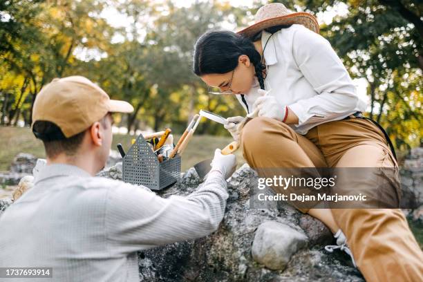 young archeologist working on the field together using magnifying glass - female-archaeologist stock pictures, royalty-free photos & images
