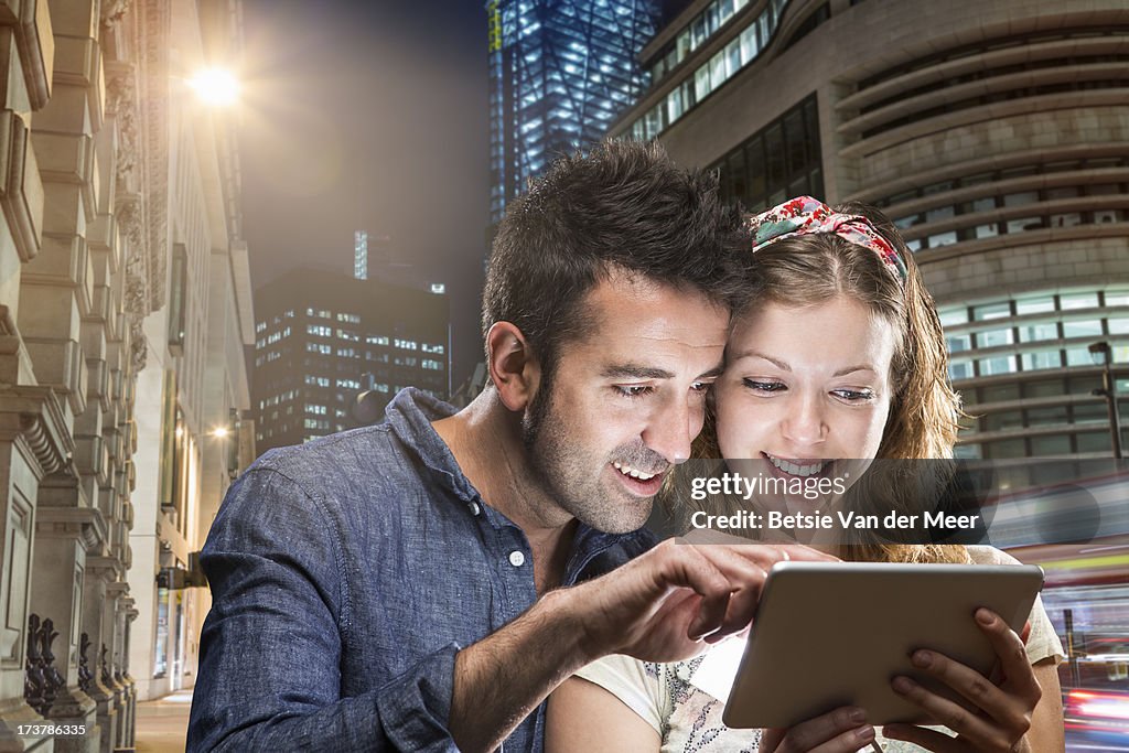 Couple looking at handheld computer device in city