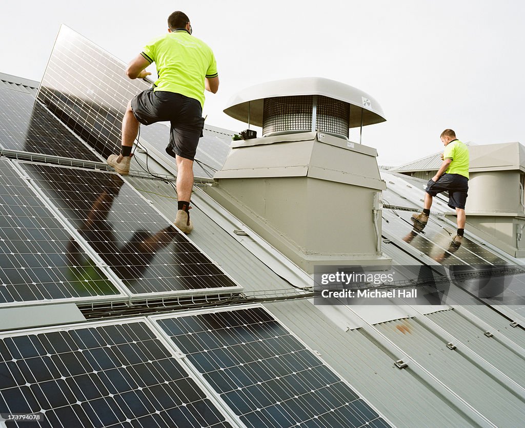 Two men installing solar panels on roof