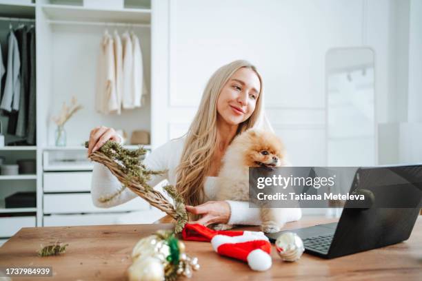holiday wreath creation: blonde woman and her spitz companion enjoy crafting a christmas wreath together, following an online tutorial. - nebenjob stock-fotos und bilder