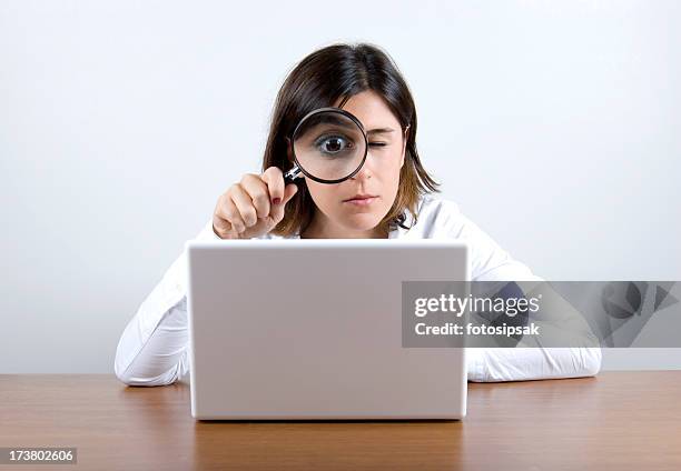 a woman holding a magnifying glass while looking at a laptop - vergrootglas stockfoto's en -beelden