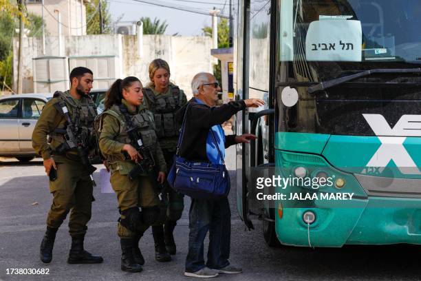 Israeli soldiers look on as a man boards a bus in the northern Israeli town of Kiryat Shmona on the border with Lebanon, before being evacuated to a...