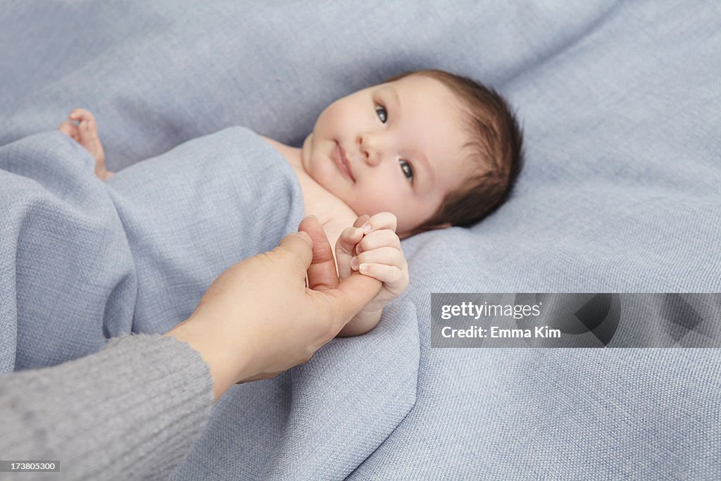 Baby boy holding mothers finger in bed