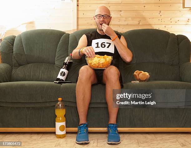 runner eating chips on sofa - laziness stock-fotos und bilder