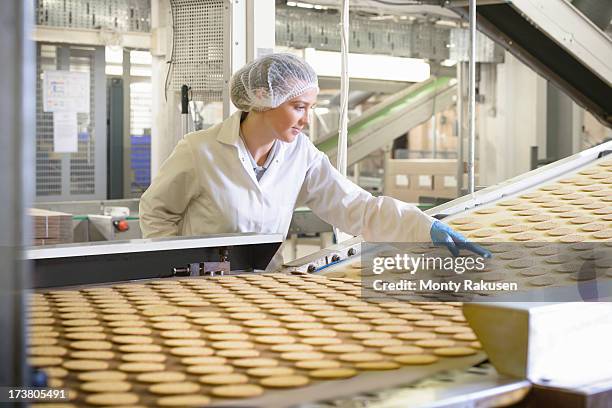 biscuit factory worker inspecting freshly made biscuits on production line - food processing plant stock pictures, royalty-free photos & images