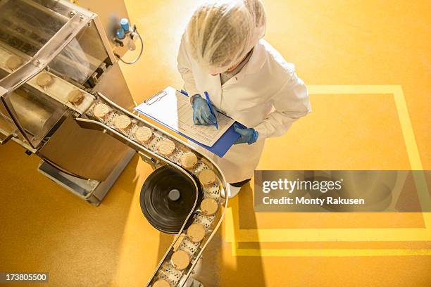 overhead view of worker inspecting biscuits on production line in food factory - nahrungsmittelfabrik stock-fotos und bilder