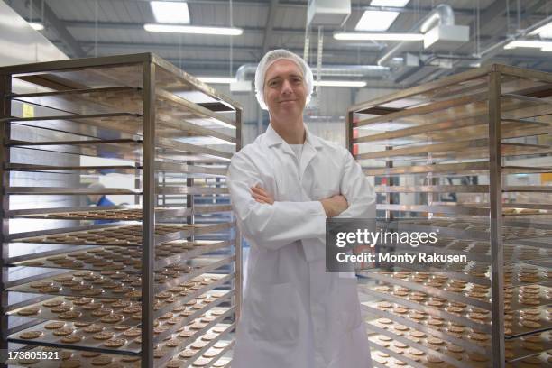 portrait of baker with trays of freshly baked biscuits in food factory - laborkittel stock-fotos und bilder