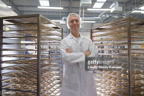 portrait of baker with trays of freshly baked biscuits in food factory - baker stock pictures, royalty-free photos & images