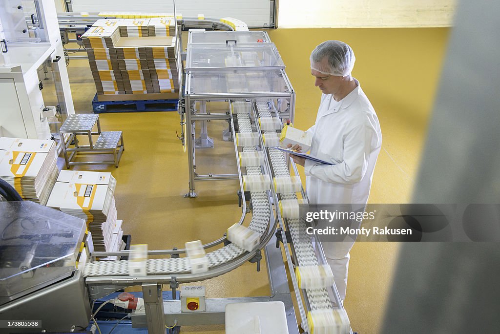 Worker inspecting packed products on conveyor belt in biscuit factory