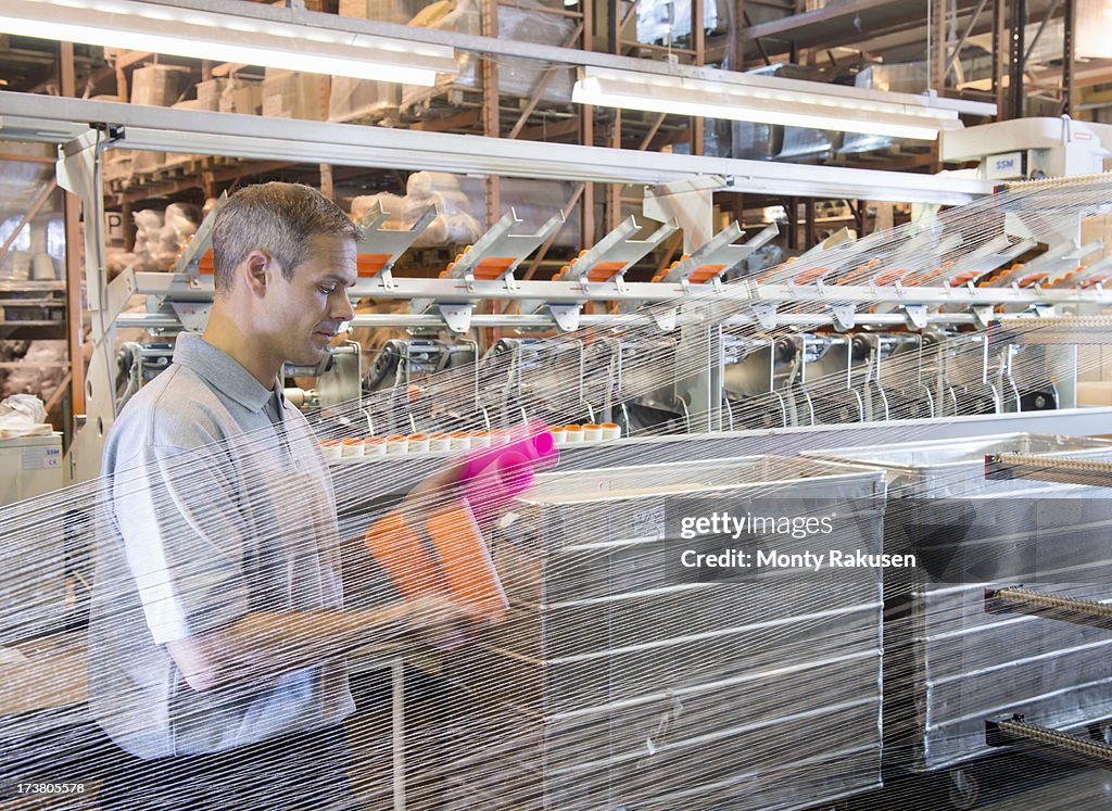 Textile worker inspecting threads on loom in mill