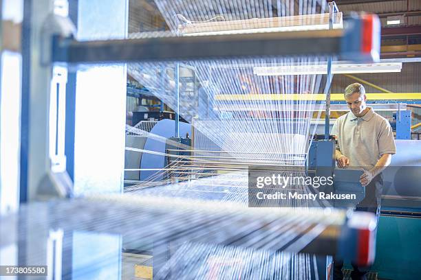 textile worker inspecting threads on loom in mill - fábrica textil fotografías e imágenes de stock